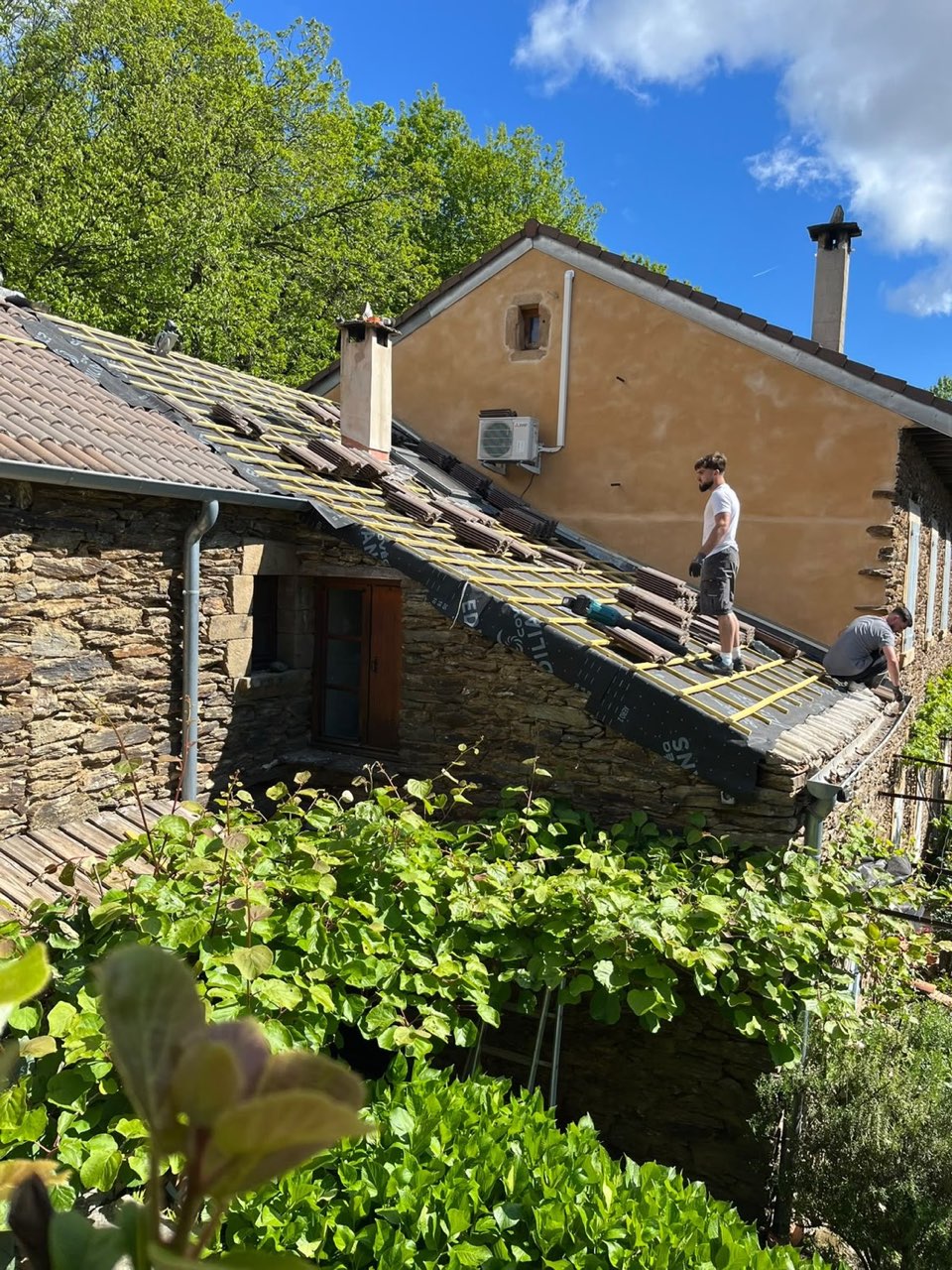Deux couvreurs de Debord Rénovation posant les liteaux et les tuiles sur une maison en pierre, en Ardèche